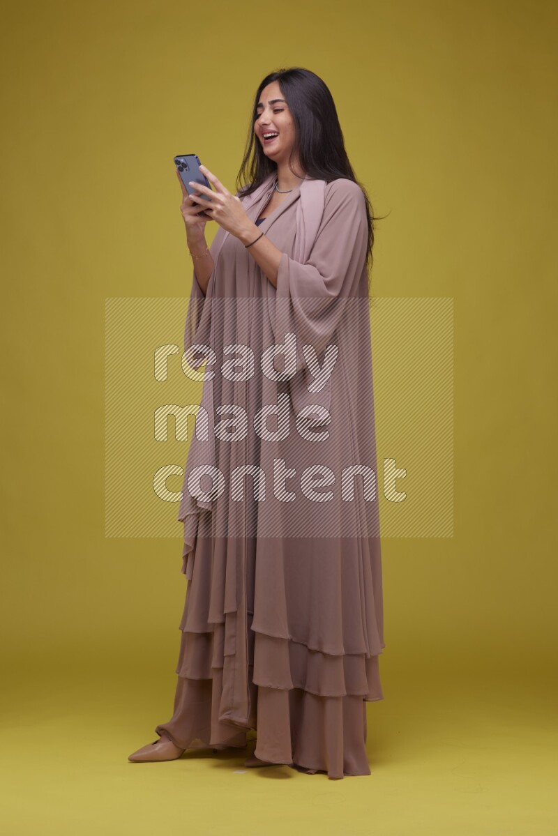 A woman Texting on a Yellow Background wearing Brown Abaya
