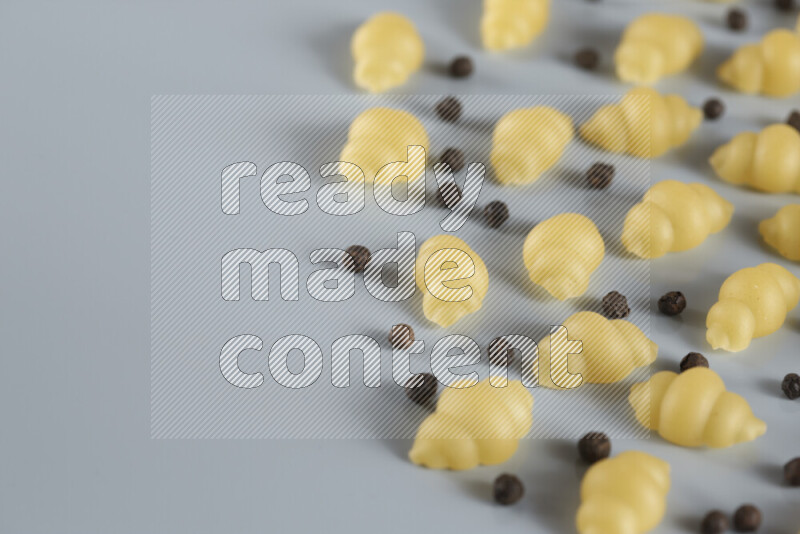 Raw pasta with different ingredients such as cherry tomatoes, garlic, onions, red chilis, black pepper, white pepper, bay laurel leaves, rosemary, cardamom and mushrooms on light blue background