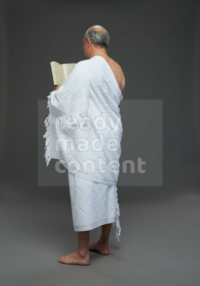 A man wearing Ehram Standing reading quran on gray background