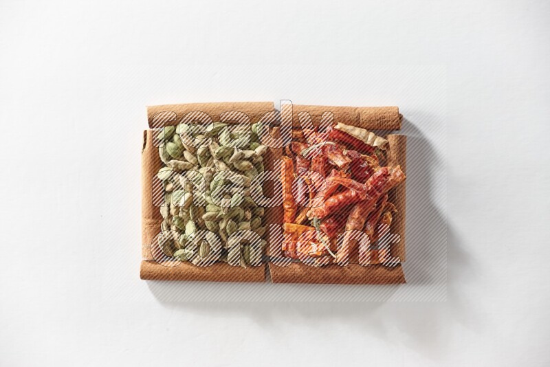 مربعان من أعواد القرفة ممتلئان بحبوب الهيل والفلفل الحار المجفف علي خلفية بيضاء