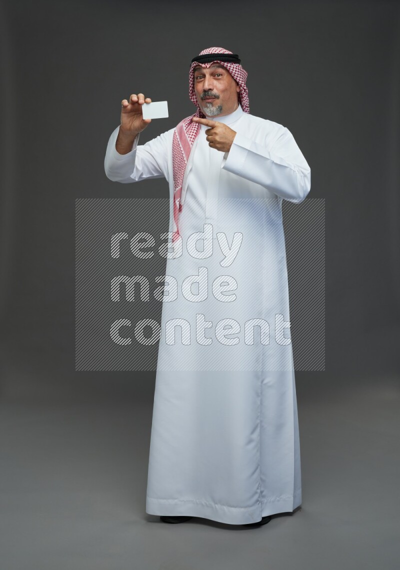 Saudi man with shomag Standing holding ATM card on gray background
