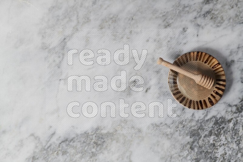 طبق فخاري متعدد الألوان مع ملعقة عسل خشبية بداخله على خلفية من الرخام الرمادي