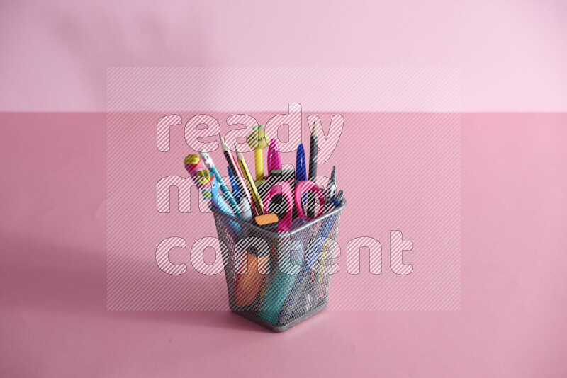 Pens, pencils and other different school supplies in a metal pen holder on rose background
