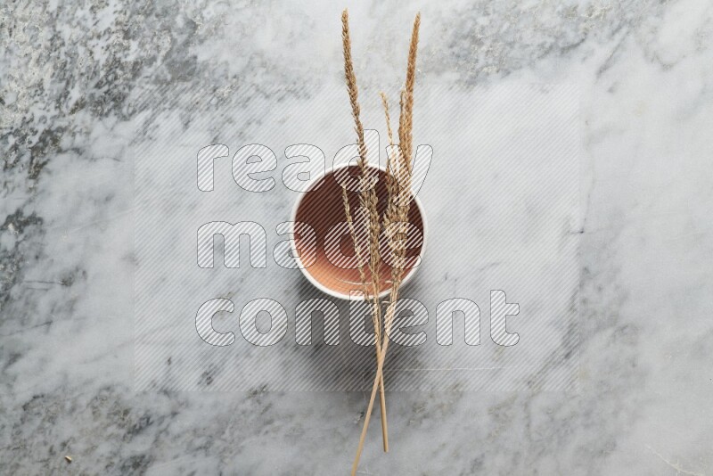 Wheat stalks on brown pottery bowl on grey marble background