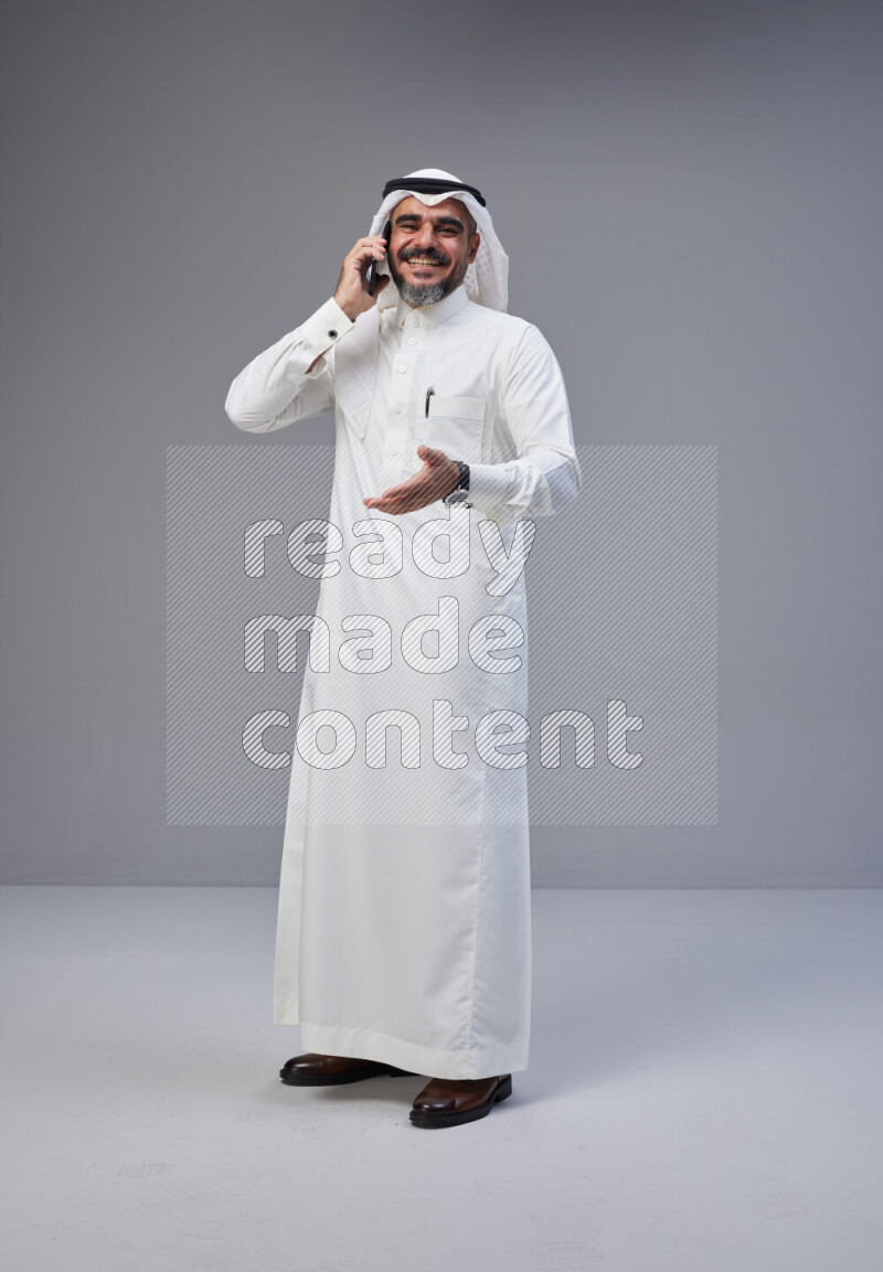 Saudi man Wearing Thob and white Shomag standing talking on phone on Gray background