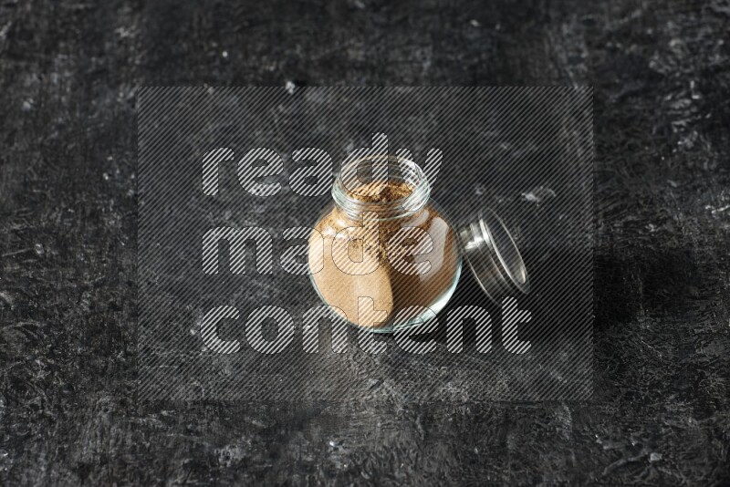 وعاء زجاجي للتوابل ممتلئ ببودرة بهار الفلفل الحلو على خلفية سوداء