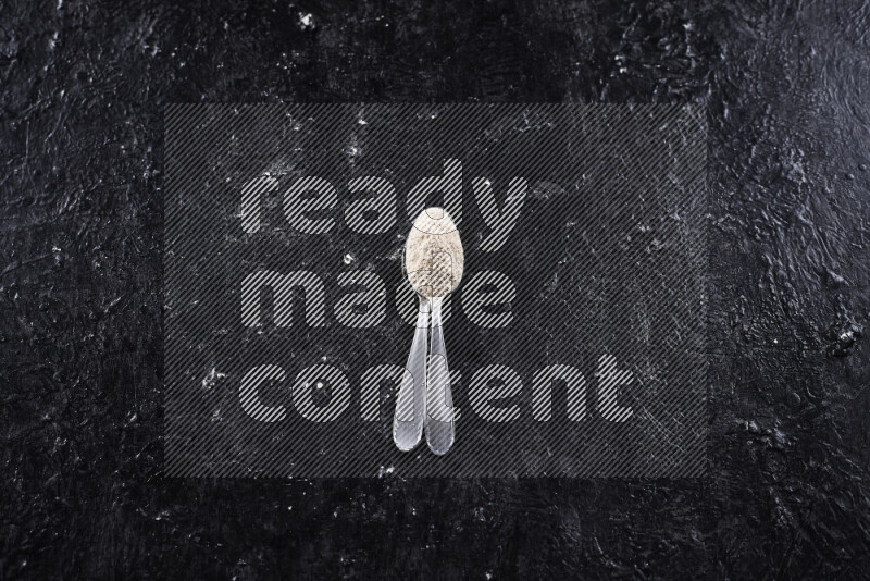 Two metal spoons full of onion powder on black background