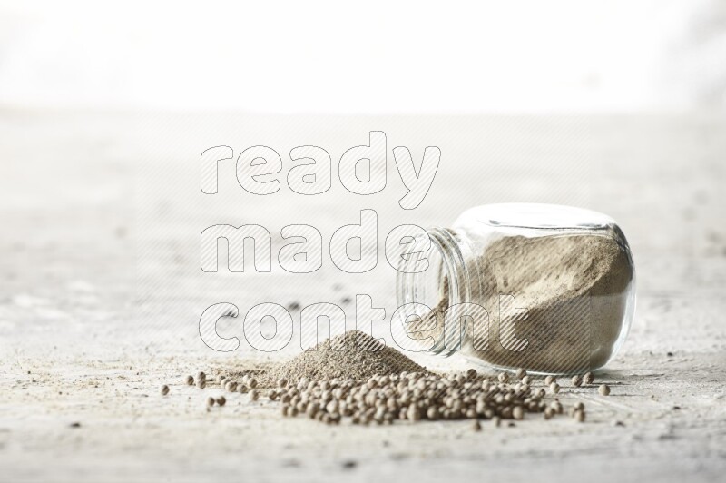 A flipped herbal glass jar full of white pepper powder with spilled powder and beads on textured white flooring
