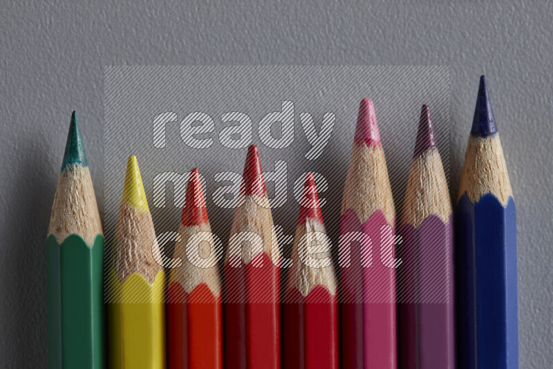 A collection of colored pencils arranged showcasing a gradient of different hues on grey background