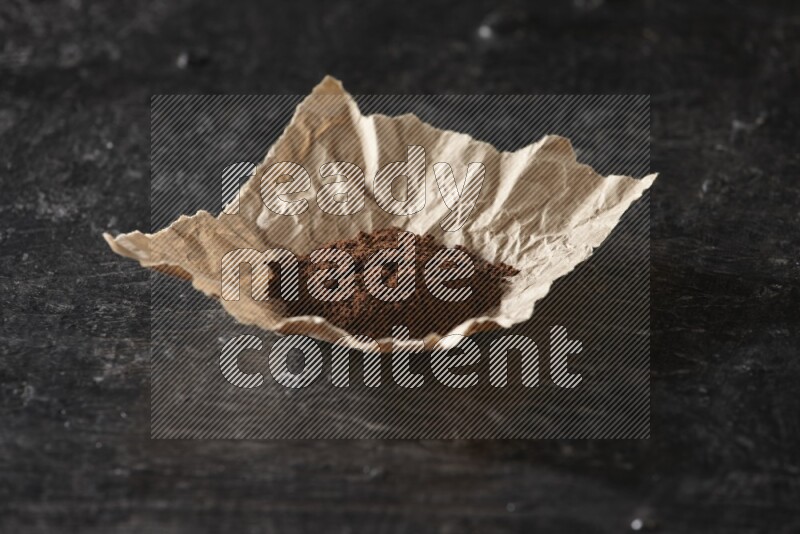 Cloves powder in crumpled piece of paper on a textured black flooring