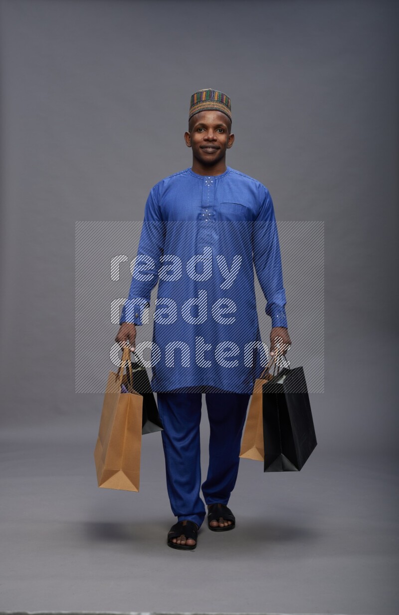 Man wearing Nigerian outfit standing holding shopping bag on gray background