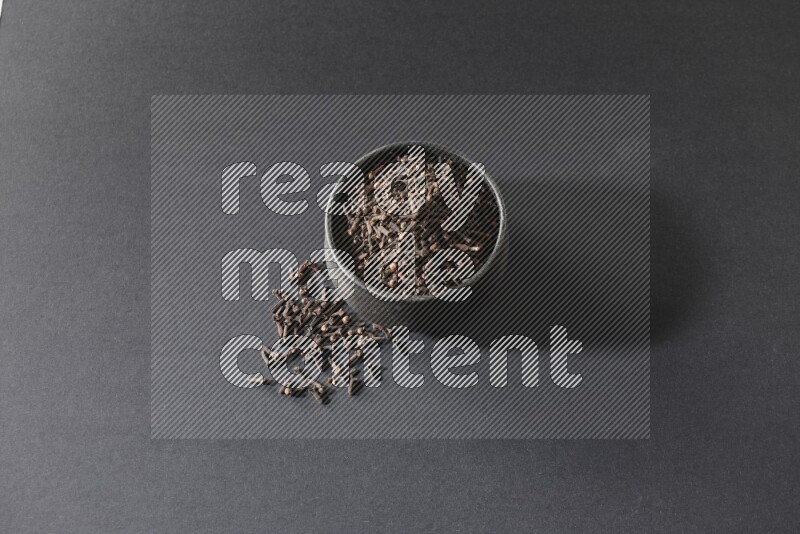 A black pottery bowl full of cloves on a black flooring
