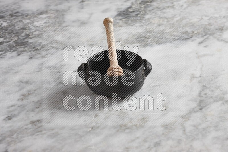 Black pottery bowl with wooden honey dipper in it on grey marble background