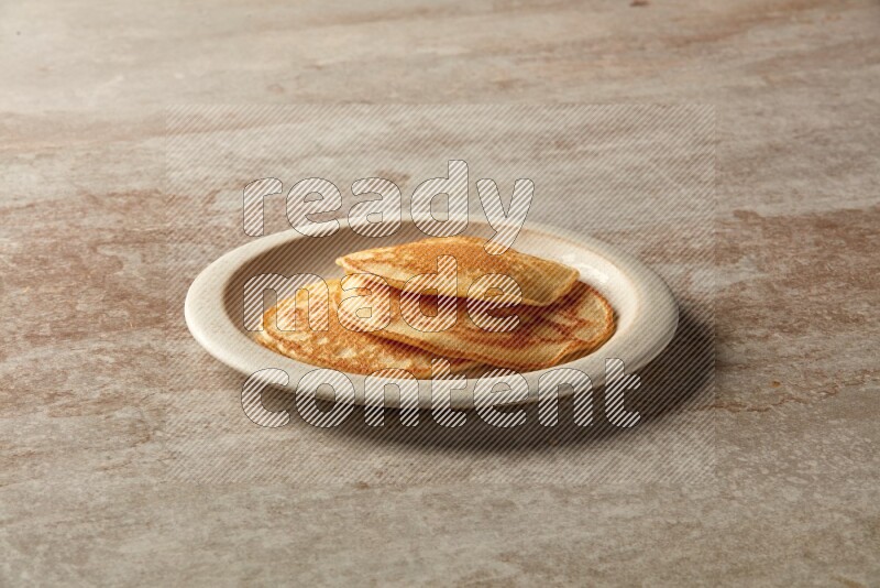 Three stacked plain pancakes in a beige plate on grey beige background