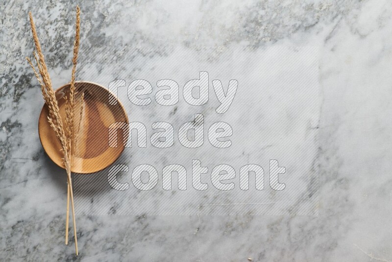 Wheat stalks on multicolored pottery plate on grey marble background