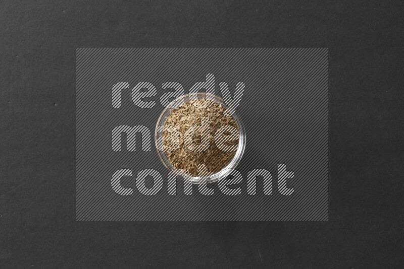 A glass bowl full of cumin on black flooring