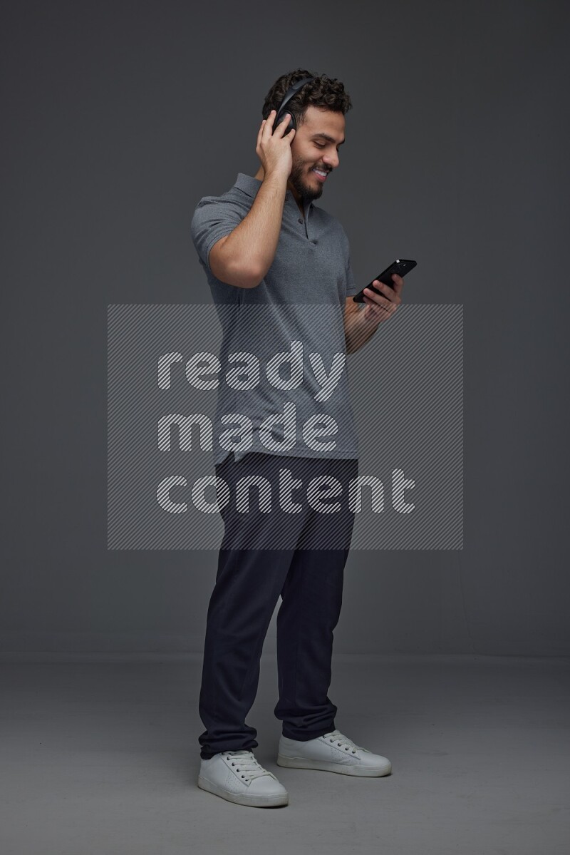 A man wearing casual and using his phone and headphone eye level on a gray background