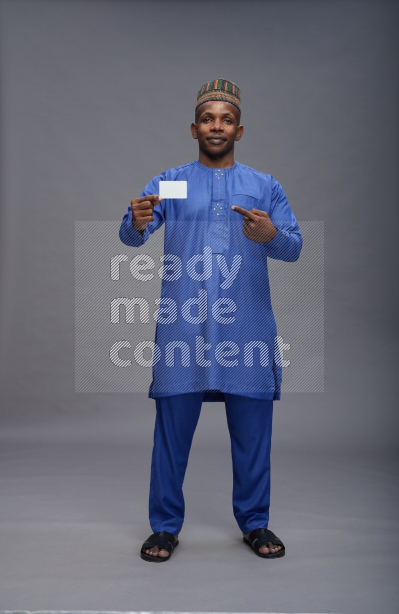 Man wearing Nigerian outfit standing holding ATM card on gray background