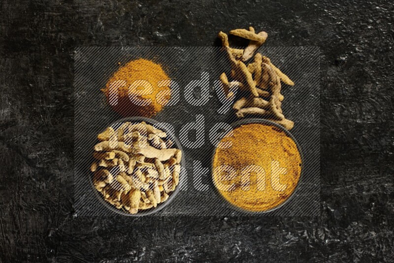 وعاءان من الفخار باللون الأسود، أحدهما ممتلئ ببودرة الكركم والآخر ممتلئ بأصابع كاملة من الكركم المجفف على خلفية سوداء