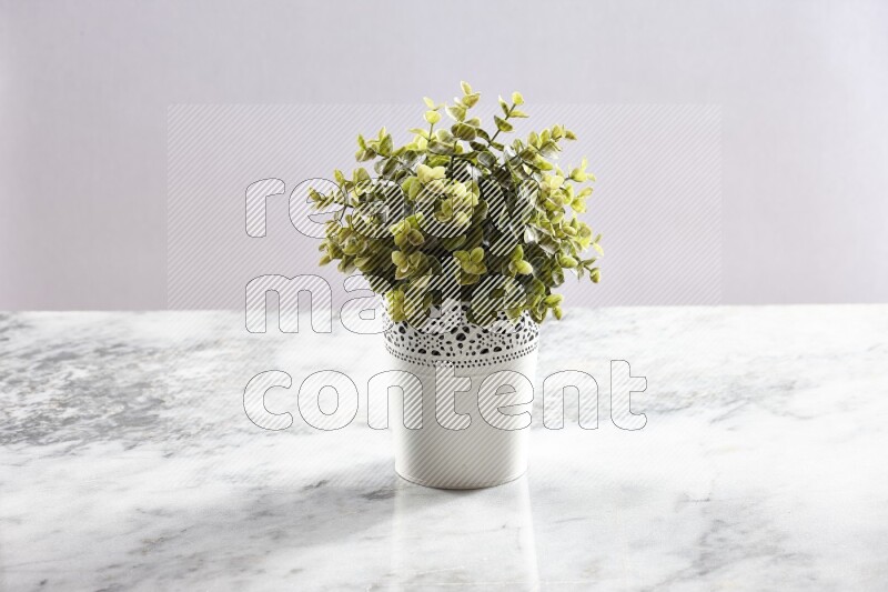 Green artificial plant in white decorative pot on grey marble background