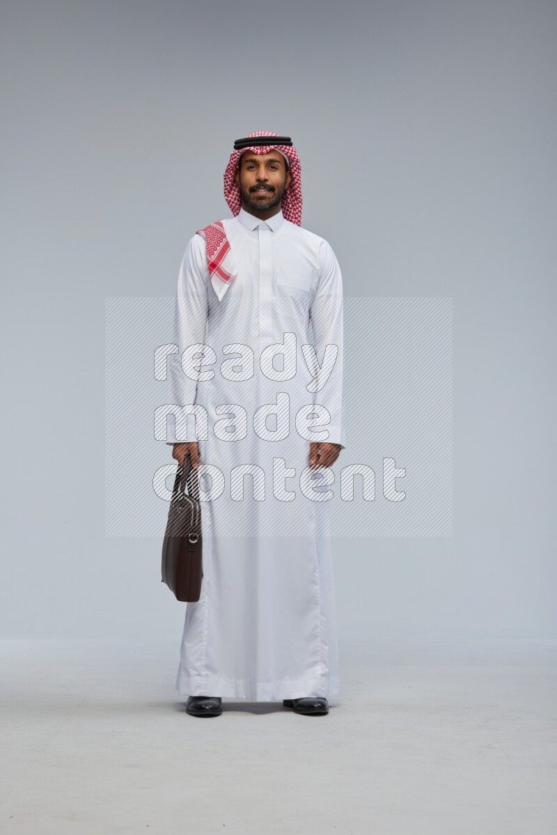 Saudi man Wearing Thob and shomag standing holding bag on Gray background