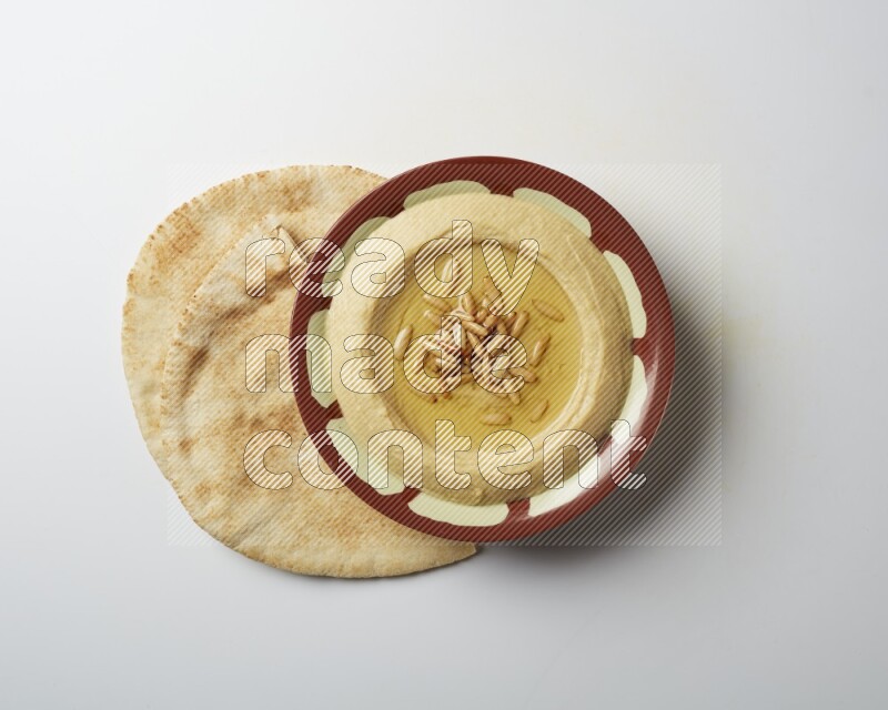 Hummus in a traditional plate garnished with pine nuts on a white background