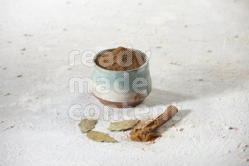 Cinnamon powder in a ceramic bowl with cinnamon sticks and laurel leaves on white background