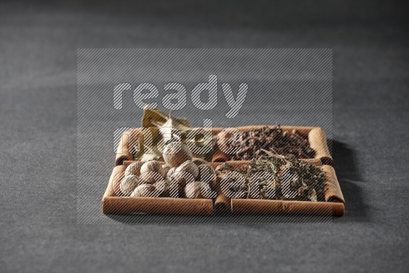 4 squares of cinnamon sticks full of bay laurel leaves, dried basil, cloves and nutmegs on black flooring