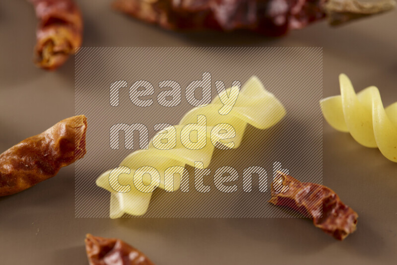 Raw pasta with different ingredients such as cherry tomatoes, garlic, onions, red chilis, black pepper, white pepper, bay laurel leaves, rosemary and cardamom on beige background