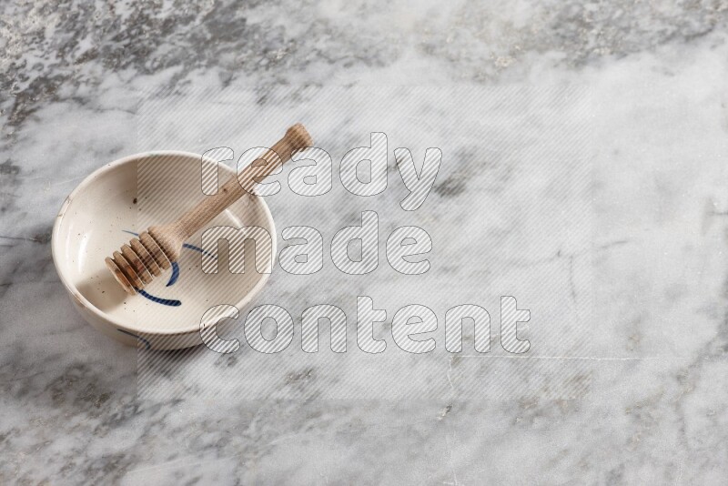 Multicolored pottery bowl with wooden honey dipper in it on grey marble background