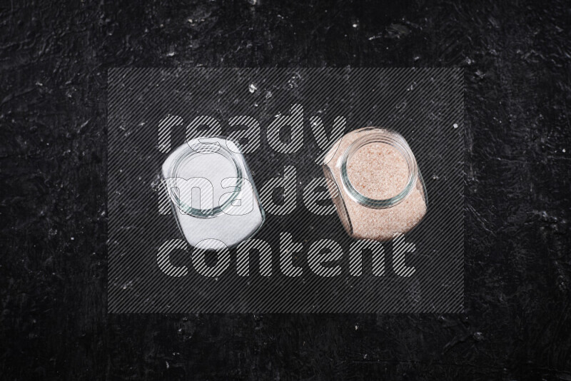 2 glass jars one is filled with fine himalayan salt and the other with table salt on black background