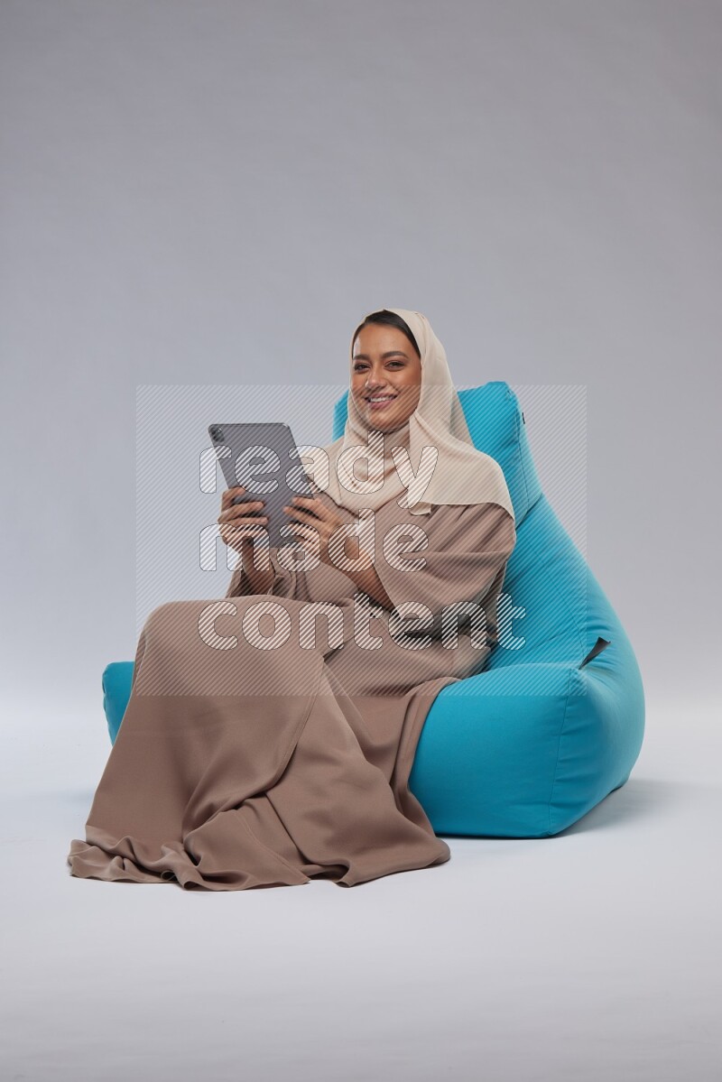 A Saudi woman sitting on a blue beanbag and working on tablet