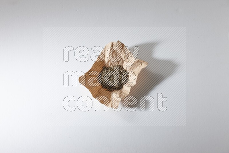 Cumin seeds in a crumpled piece of paper on white flooring