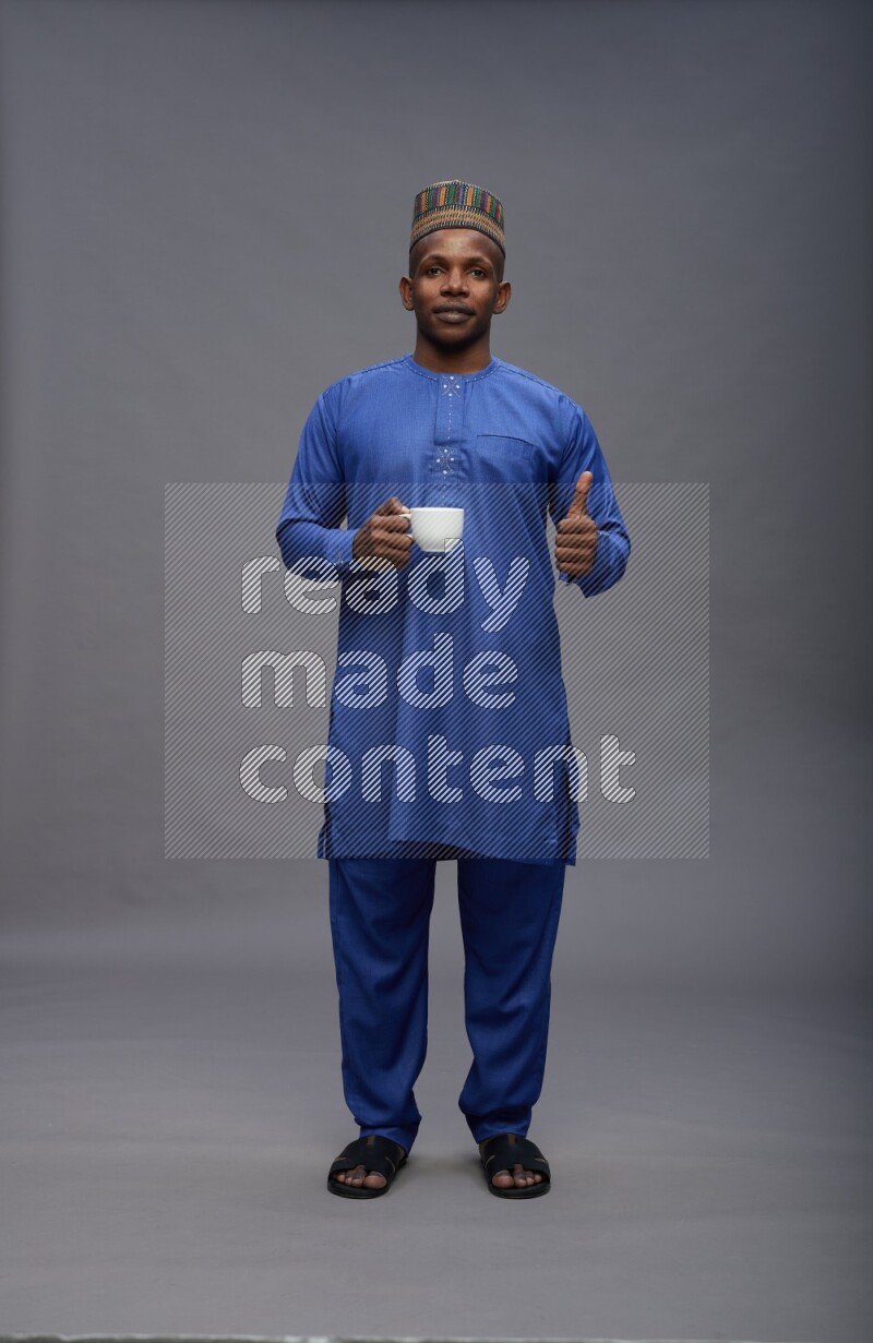 Man wearing Nigerian outfit standing holding mug on gray background