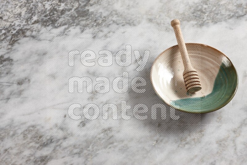 Multicolored pottery plate with wooden honey dipper in it on grey marble background