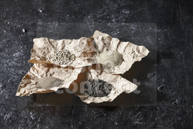 Crumpled pieces of paper full of black and white pepper beads and powder on a textured black flooring