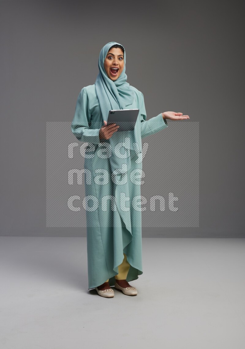 Saudi Woman wearing Abaya standing working on tablet on Gray background