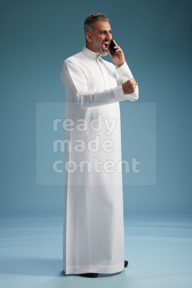 Saudi man wearing thob talking on the phone on blue background