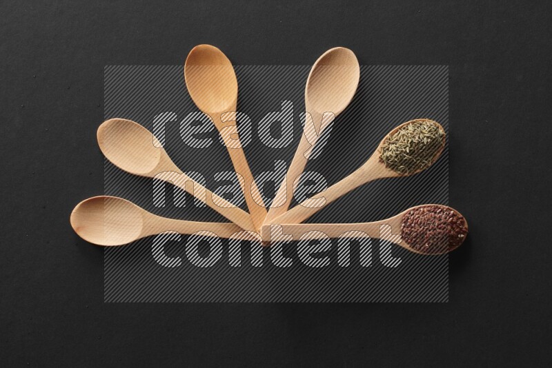 الفلفل الأسود وحبوب الخردل وحبة البركة وحب الرشاد والكمون و حبوب الكتان في معالق خشبية علي خلفية سوداء