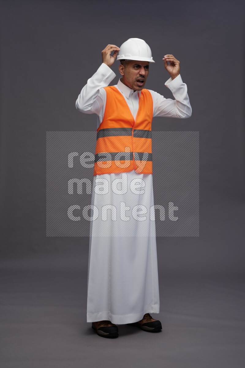 Saudi man wearing thob with engineer vest standing hands on head on gray background