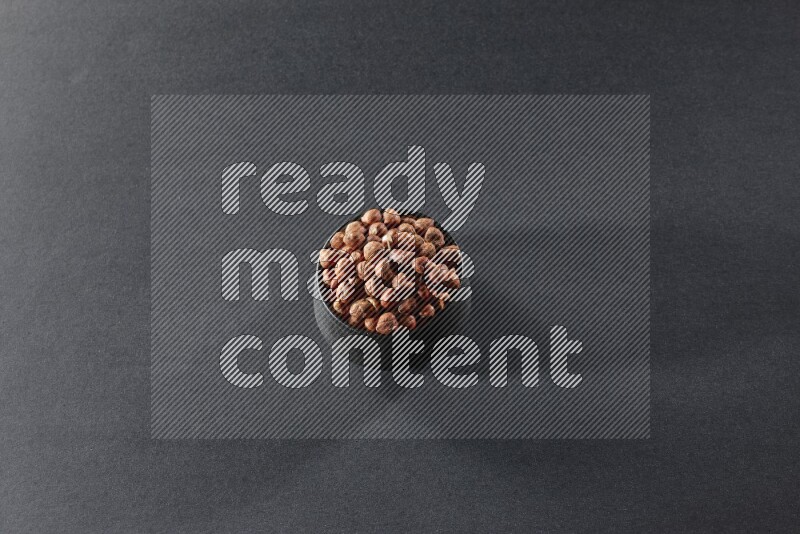 A black pottery bowl full of peeled hazelnuts on a black background in different angles