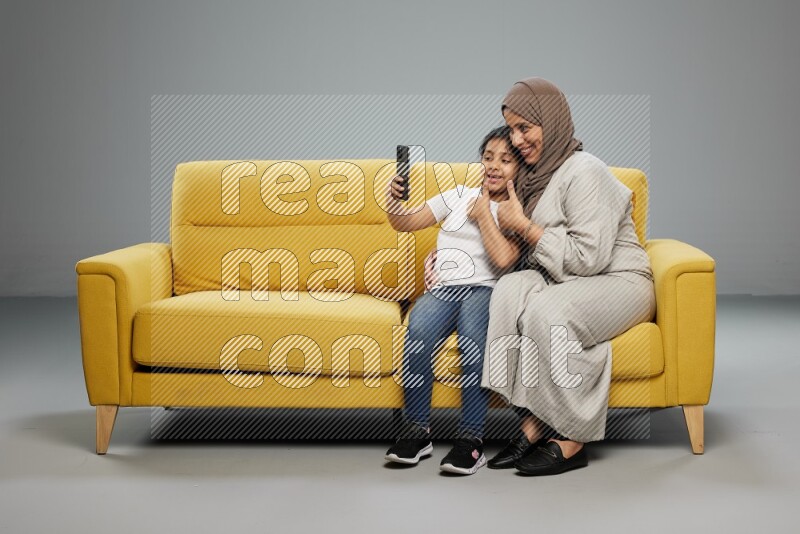 A girl sitting taking selfie with her mother on gray background