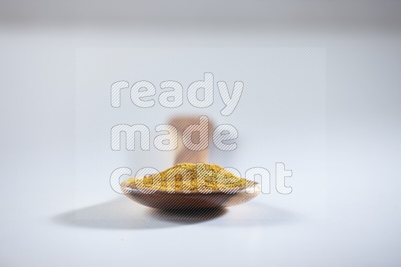 A wooden ladle full of turmeric powder on white flooring