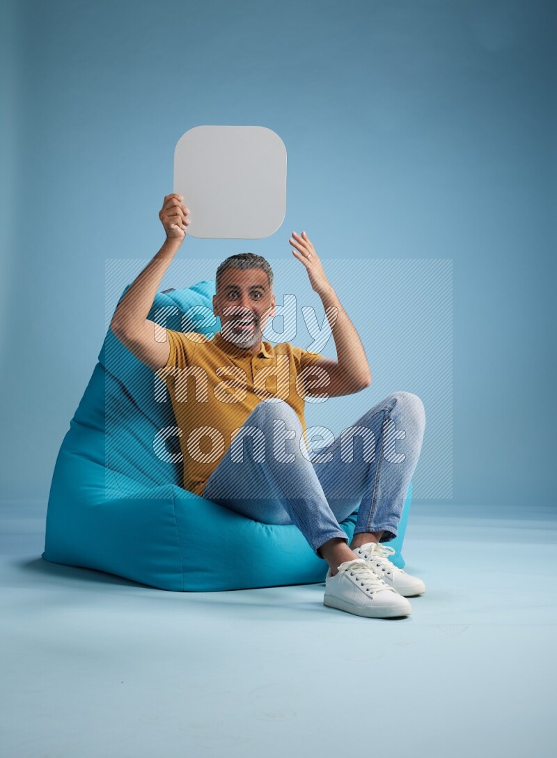 A man sitting on a blue beanbag and holding social media sign