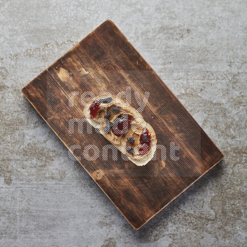 open faced peanut butter sandwich with jam and dried cranberries on a grey textured background