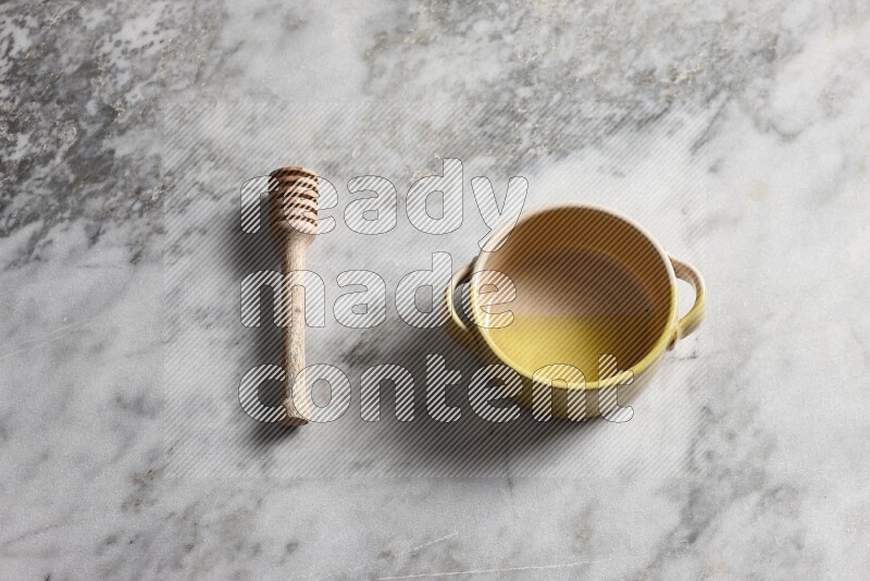 Multicolored pottery bowl with wooden honey dipper on the side on grey marble background