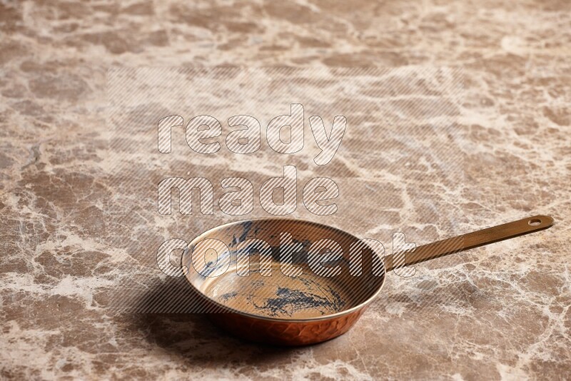 A small copper pan on beige marble background