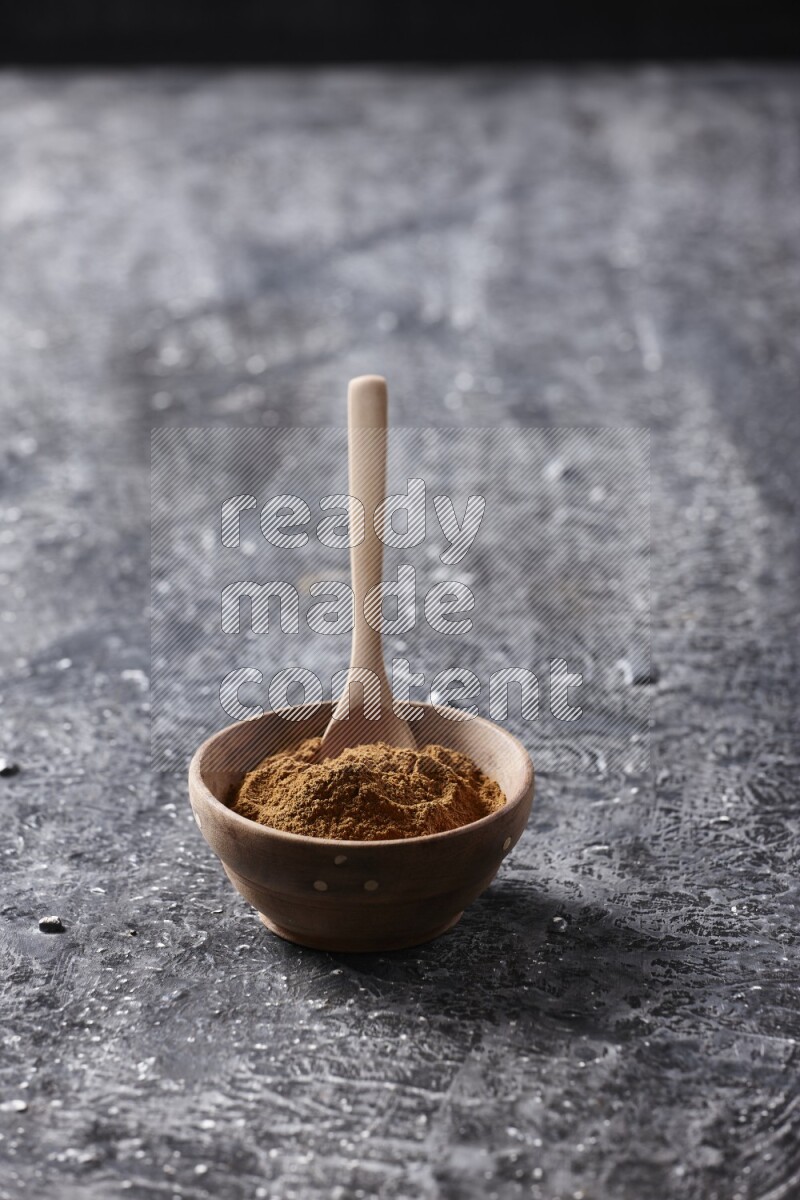 Wooden bowl full of cinnamon powder with a wooden spoon on a textured black background in different angles