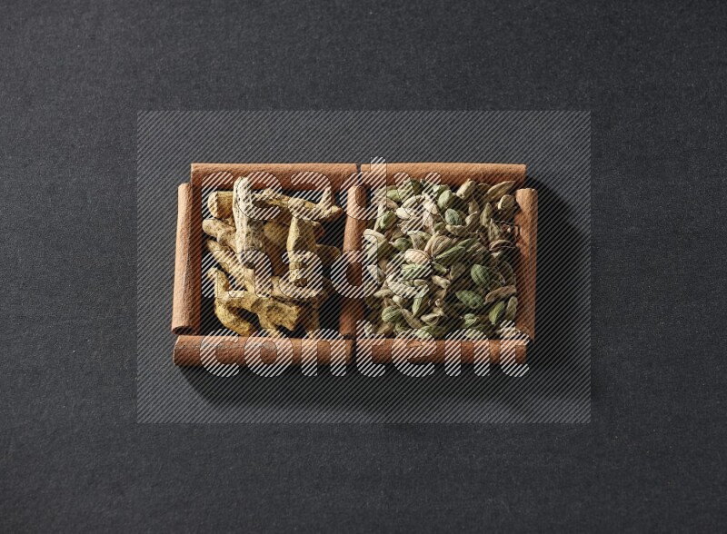 2 squares of cinnamon sticks full of cardamom and turmeric fingers on black flooring