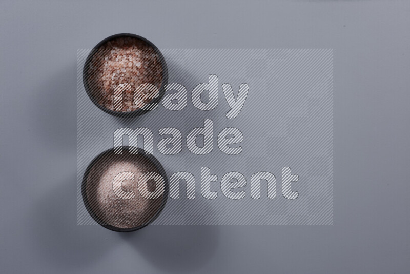 2 pottery bowls one is filled with fine himalayan salt and the other with coarse himalayan salt on grey background